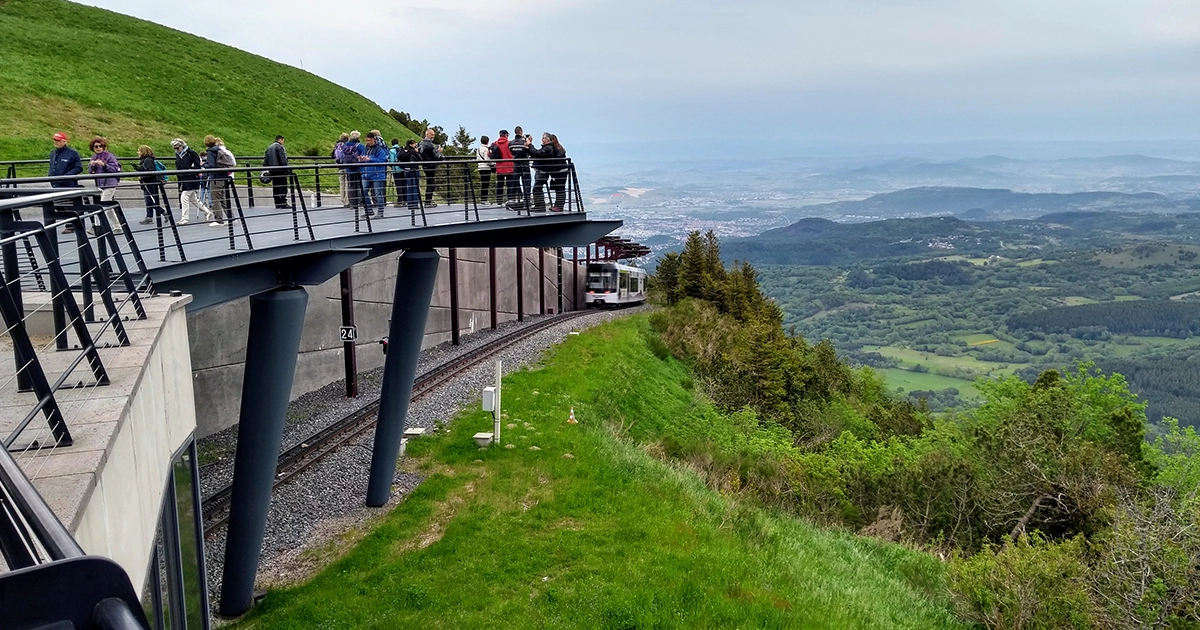 personnes se tenant sur un pont au-dessus d'une voie de chemin de fer dans les montagnes